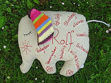 Ein grauer Stoff-Elefant, mit einem roten Stift beschriftet. In der Mitte steht „Rolf“, umrahmt von "Tänzer, Fantasie, Begeisterung, Empathie, Friese, ehrlich, fürsorglich, Humor, lustig, wertschätzend, geduldig, interessiert,…".